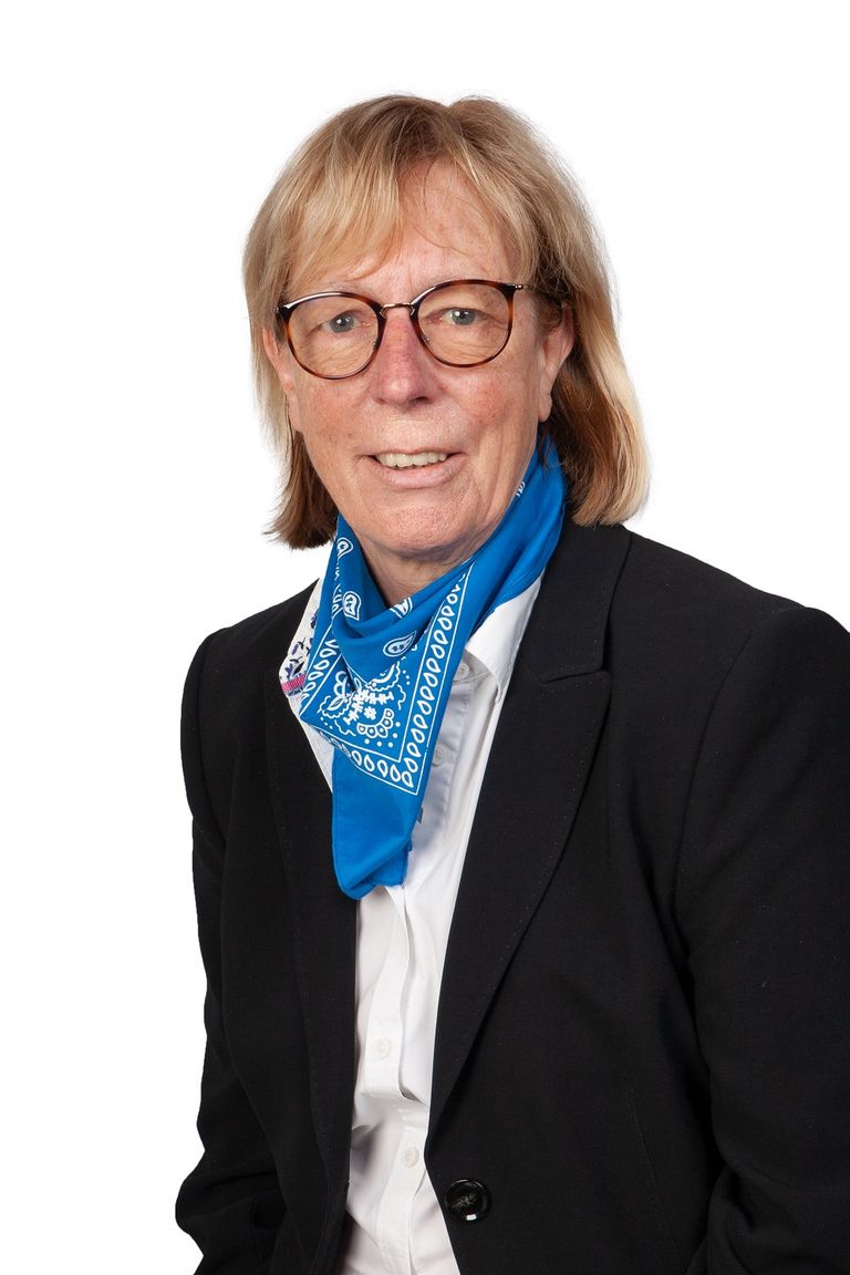 Ältere Frau mit Brille, blauem Schal und dunklem Blazer, freundlich lächelnd.