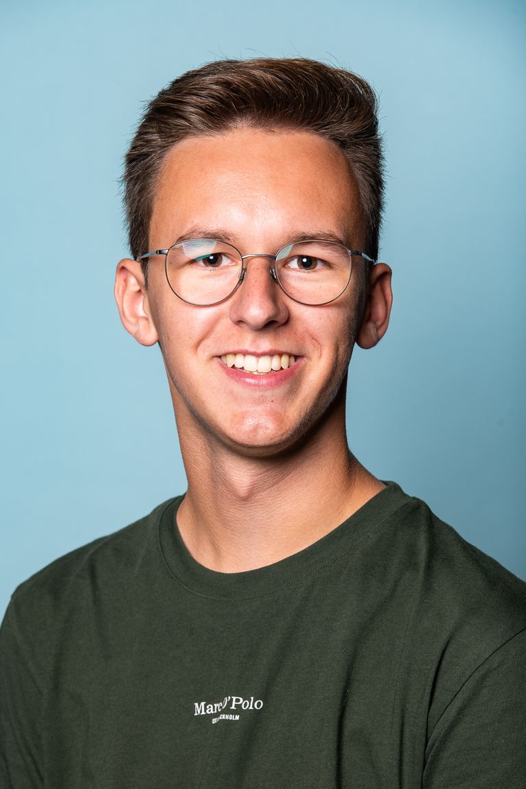 Lächelnder junger Mann mit Brille in grünem Shirt vor blauem Hintergrund.
